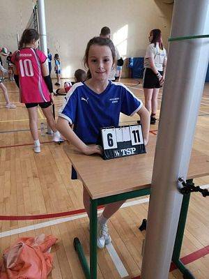 Dziewczynka w hali sportowej, stoi przy tabliczce z wynikami.