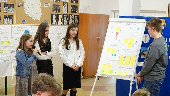 Młodzież przy tablicy typu flipchart prezentuje swoje pomysły.