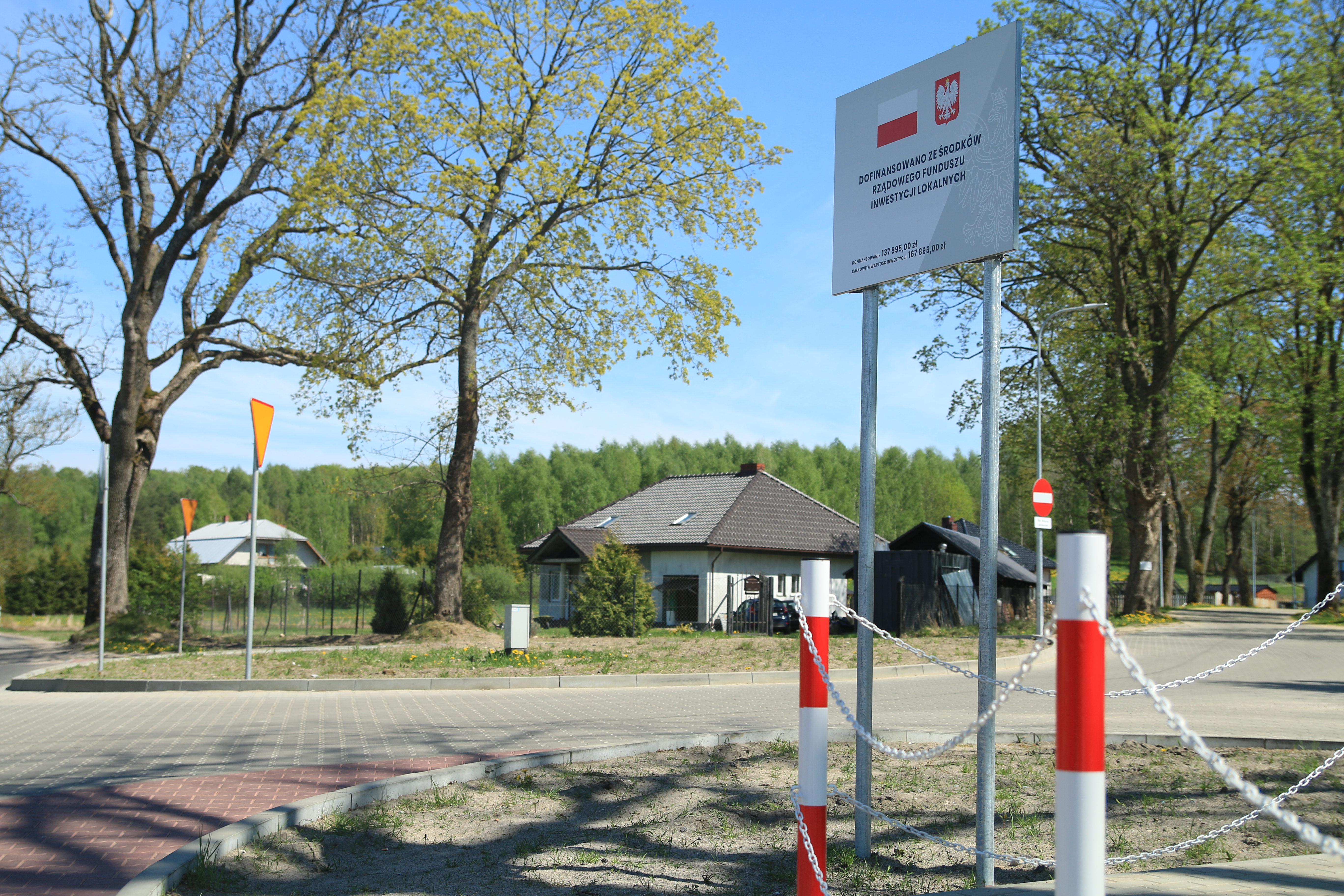 Przebudowane skrzyżowanie w Kębłowie Nowowiejskim - rondo ze zjazdem na Łowcze i zatoczką autobusową. Na pierwszym planie tablica informacyjna o dofinansowaniu z RFIL.