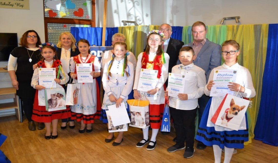 Laureaci konkursu z dyplomami i nagrodami pozują do zdjęcia. Na drugim planie jury konkursu.