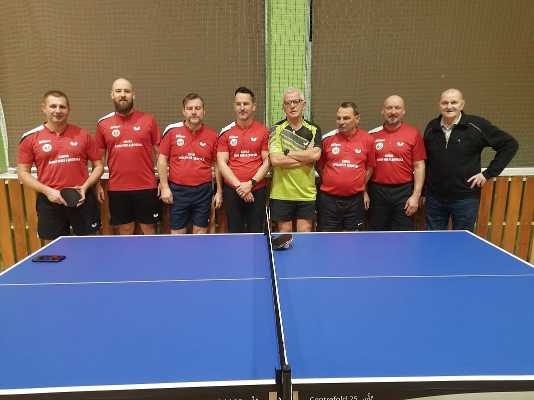 Zawodnicy GKS Tęcza stoją w rzędzie w koszulkach klubowych za stołem do tenisa stołowego.