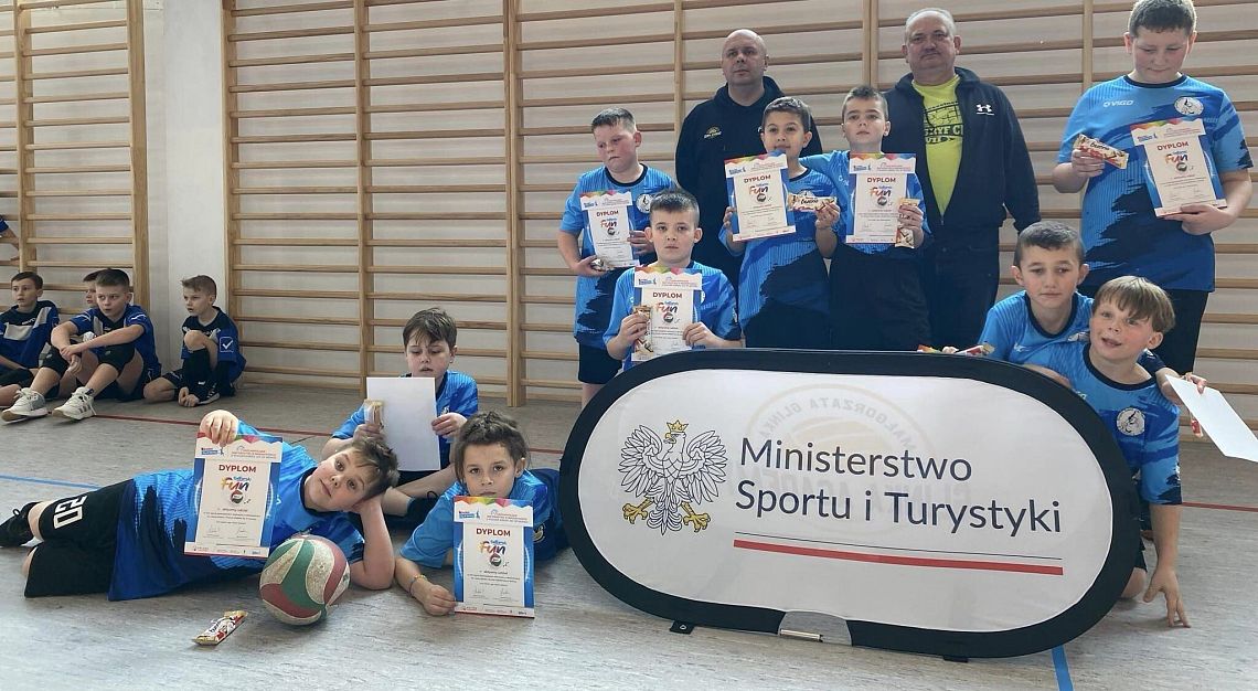 Zawodnicy z dyplomami i trenerzy pozują do pamiątkowego zdjęcia.