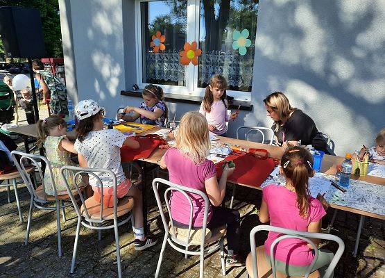 Dzieci w ogrodzie, siedzące stole ustawionym przy budynku, wykonujące prace plastyczne.