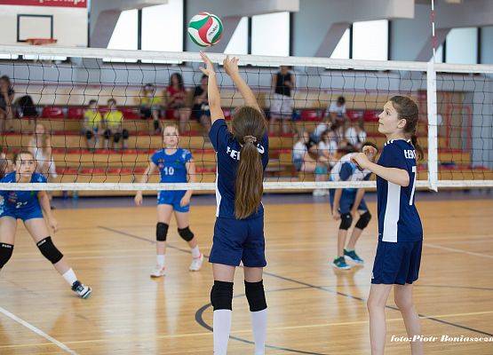 Dziewczęta w trakcie gry w piłkę siatkową w hali sportowej.