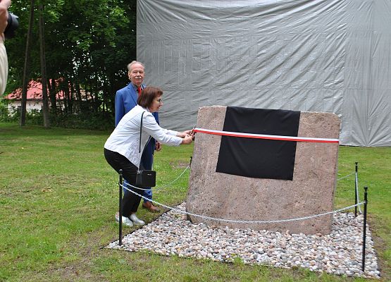 Starosta Powiatu Lęborskiego przecina wstęgę odsłaniając pamiątkową tablicę.