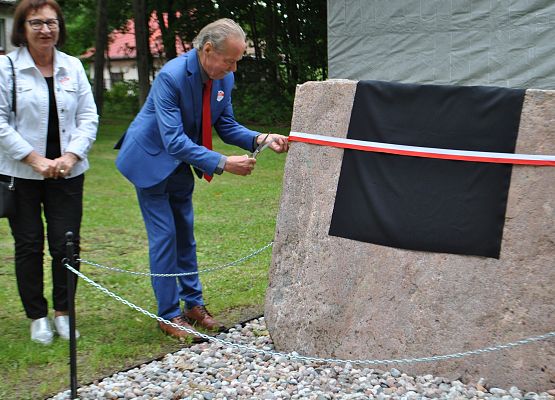 Sołtys Redkowic przecina wstęgę, odsłaniając pamiątkową tablicę.