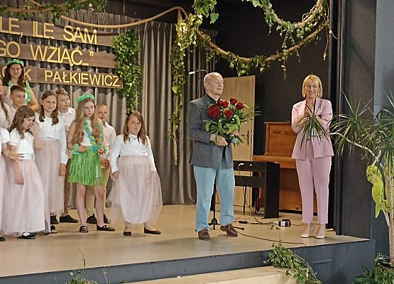 Na scenie w obecności uczniów dyrektor szkoły w Mostach składa życzenia Jackowi Pałkiewiczowi.
