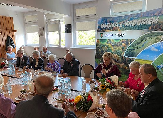 Jubilaci, wójt, zaproszeni goście siedzą przy wspólnym stole przy kawie i torcie.