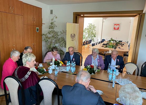 Jubilaci, wójt, zaproszeni goście siedzą przy wspólnym stole przy kawie i torcie.