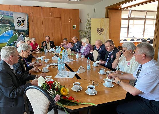Jubilaci, wójt, zaproszeni goście siedzą przy wspólnym stole przy kawie i torcie.