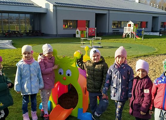 Przedszkolaki ustawione przy zabawkach na placu przy przedszkolu.