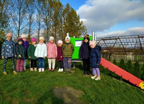 Przedszkolaki ustawione przy zjeżdżalni na placu zabaw.