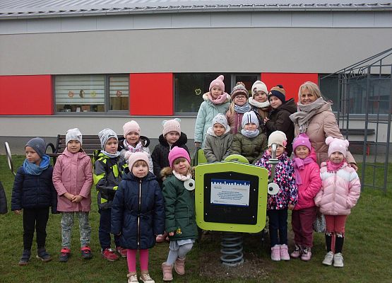 Przedszkolaki ustawione przy zabawkach na placu przy przedszkolu.