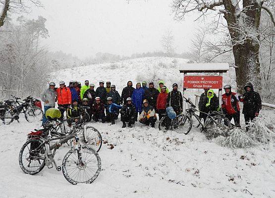 Uczestnicy rowerowej trasy rajdu pozują do zdjęcia w zimowej scenerii lasu.