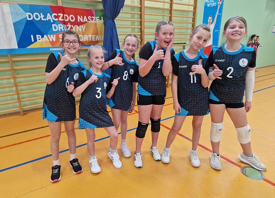 Grupa dziewczynek pozuje do zdjęcia w sali gimnastycznej.