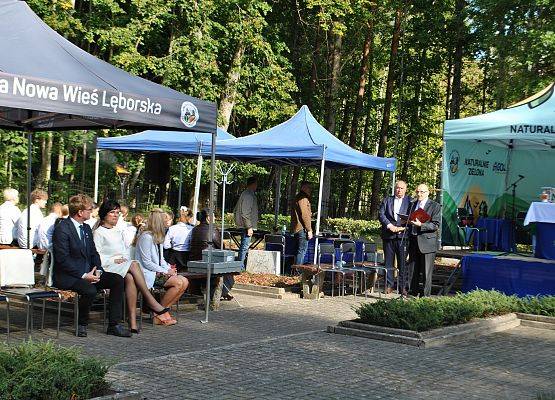 Zaproszeni goście siedzą na ławkach pod namiotem, na placu cmentarza w Krępie Kaszubskiej.