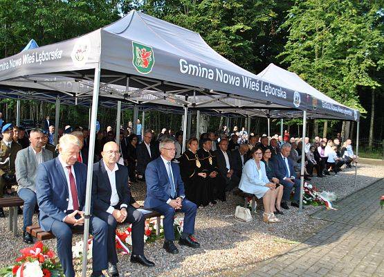 Zaproszeni goście siedzą na ławkach pod namiotem, na placu cmentarza w Krępie Kaszubskiej.