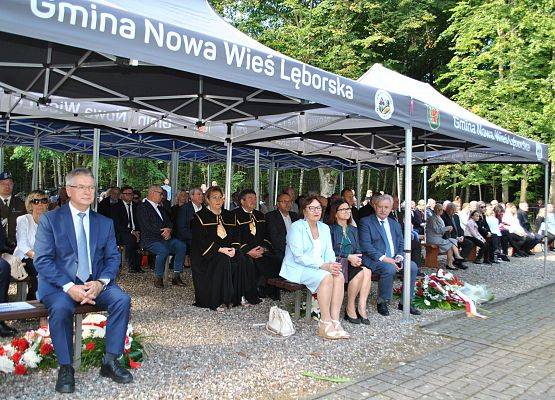 Zaproszeni goście siedzą na ławkach pod namiotem, na placu cmentarza w Krępie Kaszubskiej.