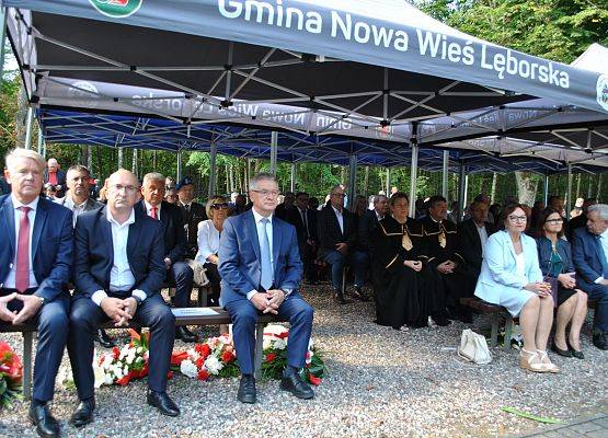 Zaproszeni goście siedzą na ławkach pod namiotem, na placu cmentarza w Krępie Kaszubskiej.