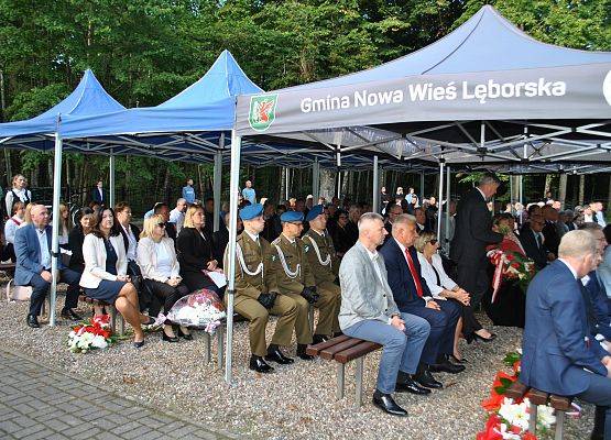 Zaproszeni goście siedzą na ławkach pod namiotem, na placu cmentarza w Krępie Kaszubskiej.