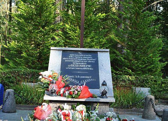Pomnik zbiorowy pomordowanych więźniów na cmentarzu w Krępie Kaszubskiej obłożony wiązankami i wieńcami kwiatów.