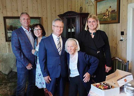 Wspólne zdjęcie wójta gminy, jubilatki i zaproszonych gości w domu jubilatki.