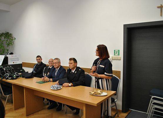 Trzech przedstawicieli OSP, Wójt gminy siedzą za stołem prezydialnym. Przedstawicielka Urzędu Marszałkowskiego w Gdańsku przemawia.