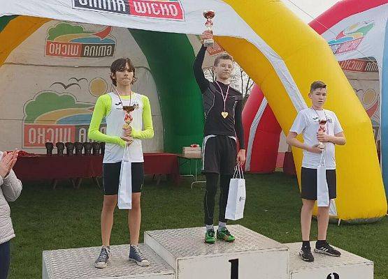 Trzej zawodnicy z pucharami stoją na podium.