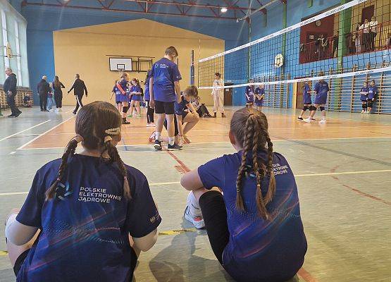 Dzieci grają w piłkę siatkową w sali gimnastycznej.