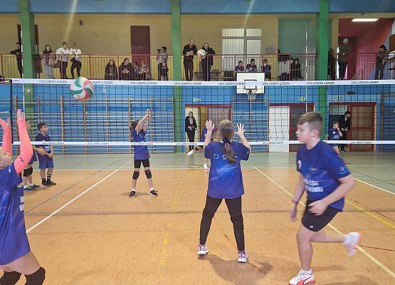 Dzieci grają w piłkę siatkową w sali gimnastycznej.