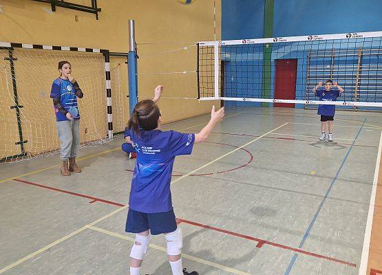 Dzieci grają w piłkę siatkową w sali gimnastycznej.