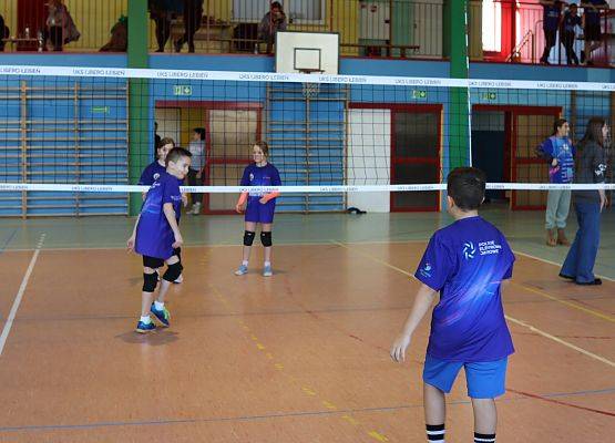 Dzieci grają w piłkę siatkową w sali gimnastycznej.