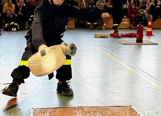 Zawodnik biegnie w wężem strażackim do kolejnej przeszkody.