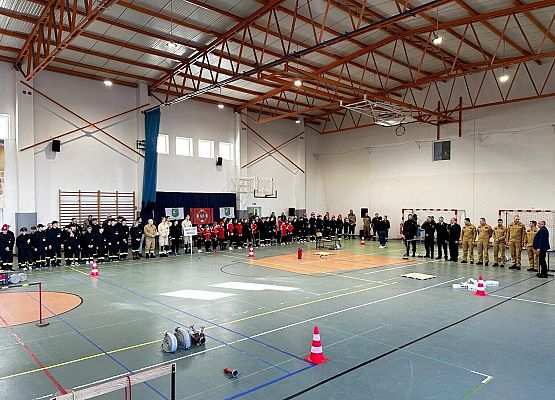 Drużyny pożarnicze i zaporszeni goście w hali sportowej.
