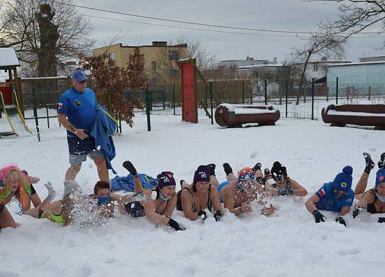 Morsing na śniegu. Grupa kilkunastu osób w strojach kąpielowych, leżących na śniegu.
