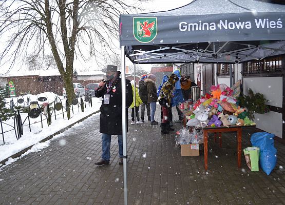 Teren rekreacyjny przed gminnym ośrodkiem kultury. Prowadzący i stoiska kiermaszowe w zimowej scenerii.