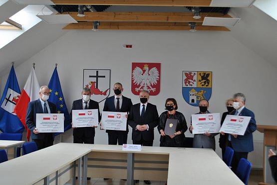 Włodarze powiatu lęborskiego i Wojewoda Pomorski po podpisaniu umów stojący w rzędzie z tabliczkami informującymi o dofinansowaniu zadań z Rządowego Funduszu Rozwoju Dróg.