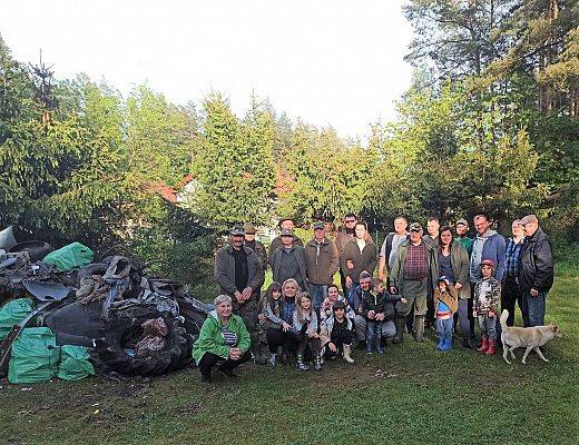 Grupa 25 uczestników akcji ustawionych na tle lasu, przy zebranych workach śmieci.