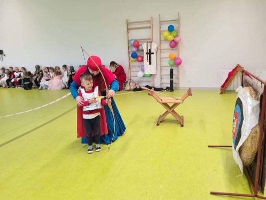 Chłopiec przy pomocy osoby dorosłej strzela z łuku do tarczy.