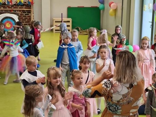 Dzieci tańczą z panią dyrektor na balu trzymając się za ręce.