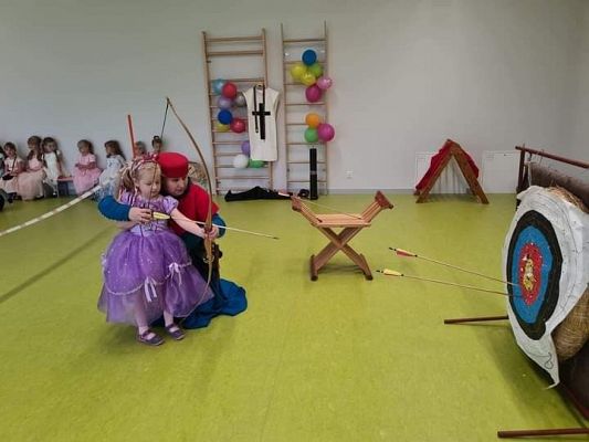 Dziewczynka przy pomocy osoby dorosłej strzela z łuku do tarczy.