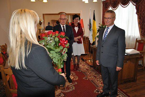 Dyrektorzy placówek oświatowych wręczają bukiet czerwonych róż wójtowi.