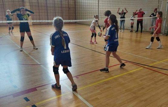 Dwie dziewczynki w trakcie gry w piłkę siatkową w hali sportowej.