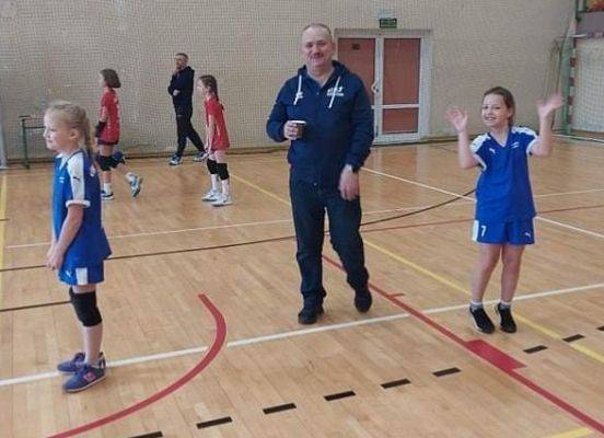 Dwie dziewczynki w trakcie gry w piłkę siatkową w hali sportowej.