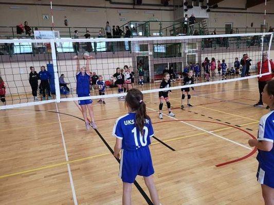 Dwie dziewczynki w trakcie gry w piłkę siatkową w hali sportowej.