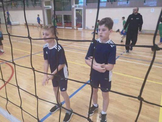 Dwóch chłopców w trakcie gry w piłkę siatkową w hali sportowej.