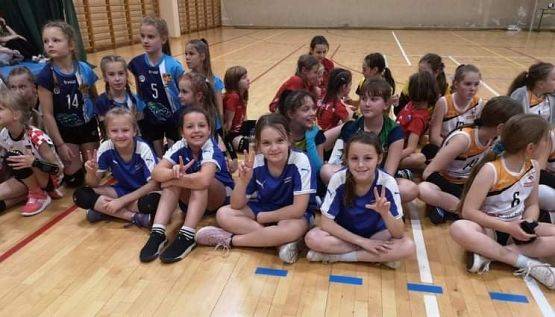 Zdjęcie grupowe. Zawodnicy i  zawodniczki siedzą na parkiecie. Na pierwszym planie zawodniczki z UKS Libero-Łebień.