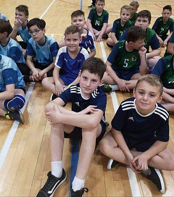 Zdjęcie grupowe. Zawodnicy i  zawodniczki siedzą na parkiecie. Na pierwszym planie zawodnicy z UKS Libero-Łebień.