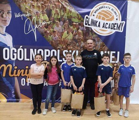 Zawodnicy i zawodniczki z trenerem i nagrodami zadowoleni pozują do zdjęcia.