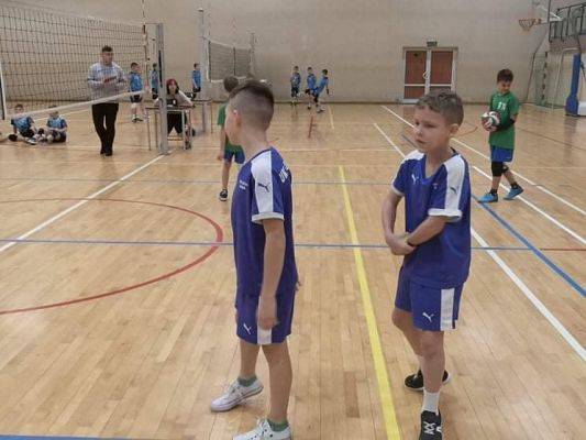 Dwóch chłopców w trakcie gry w piłkę siatkową w hali sportowej.